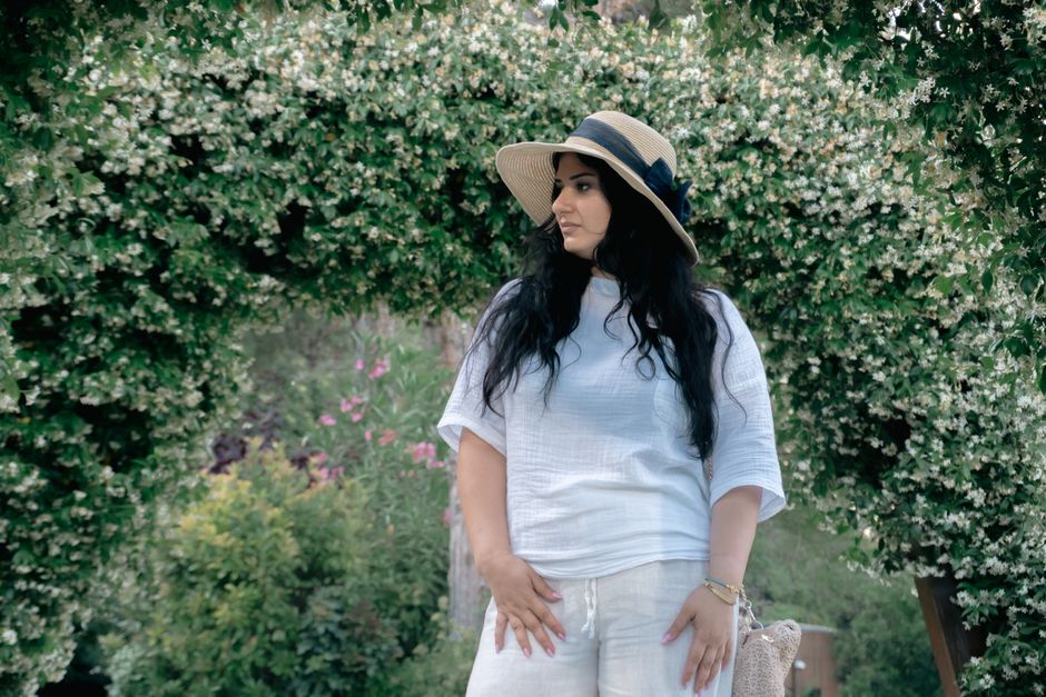 Portrait of a woman in white outfit and hat surrounded by vibrant garden flowers in Baku.