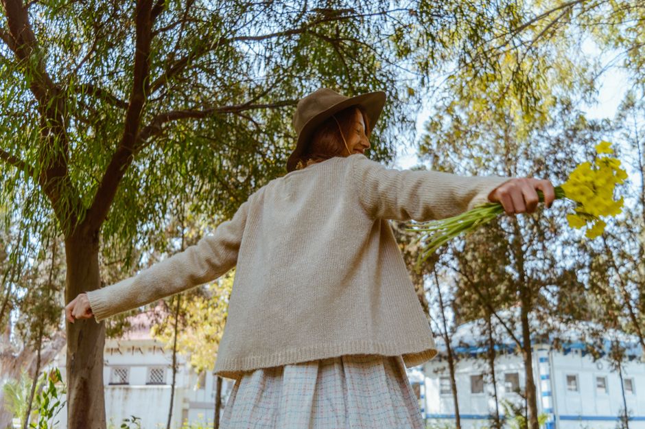 A woman in a cowboy hat enjoys freedom in a sunny park, holding yellow flowers.