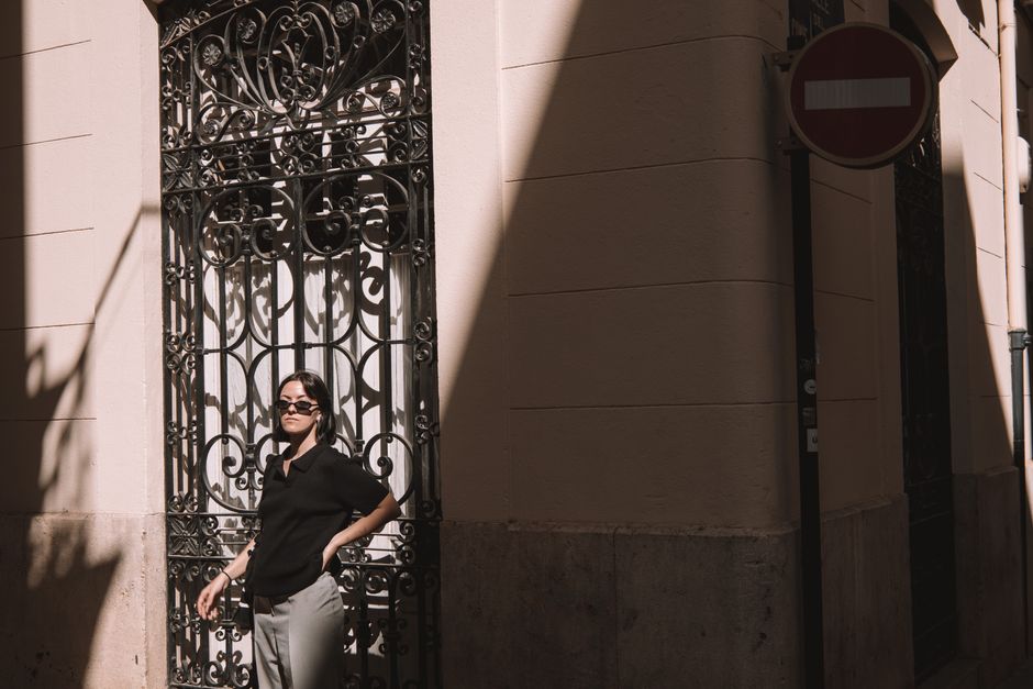 Fashionable woman in black polo posing with sunglasses on a sunny street in Valencia, Spain.