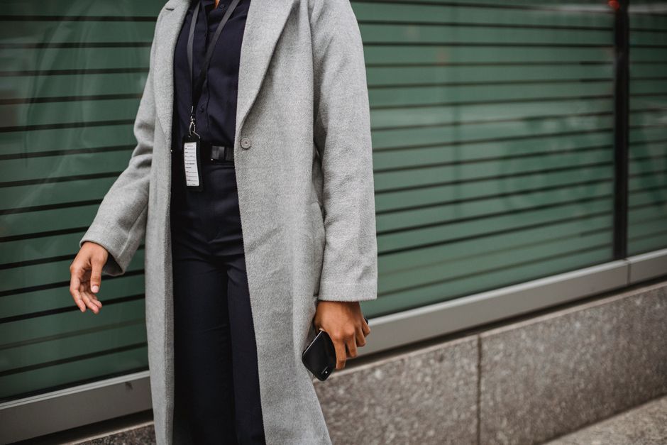 Crop unrecognizable ethnic female office employee with badge and cellphone near urban wall in daylight