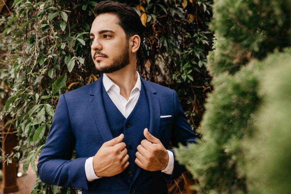 Portrait of a stylish man in a blue suit posing confidently outdoors among green plants.
