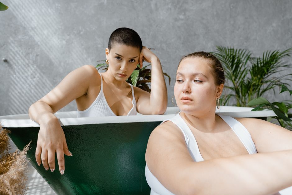 Two women enjoying leisure time in a bathtub indoors, surrounded by plants.