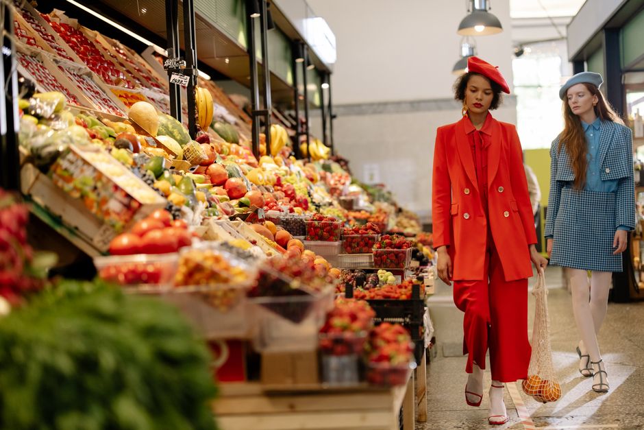 Fashionable women in vibrant outfits shopping for fresh produce in a lively supermarket.