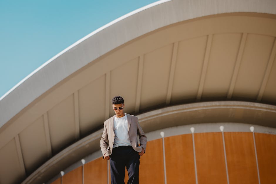 Man in stylish attire standing in front of Berlin's iconic architecture on a sunny day.