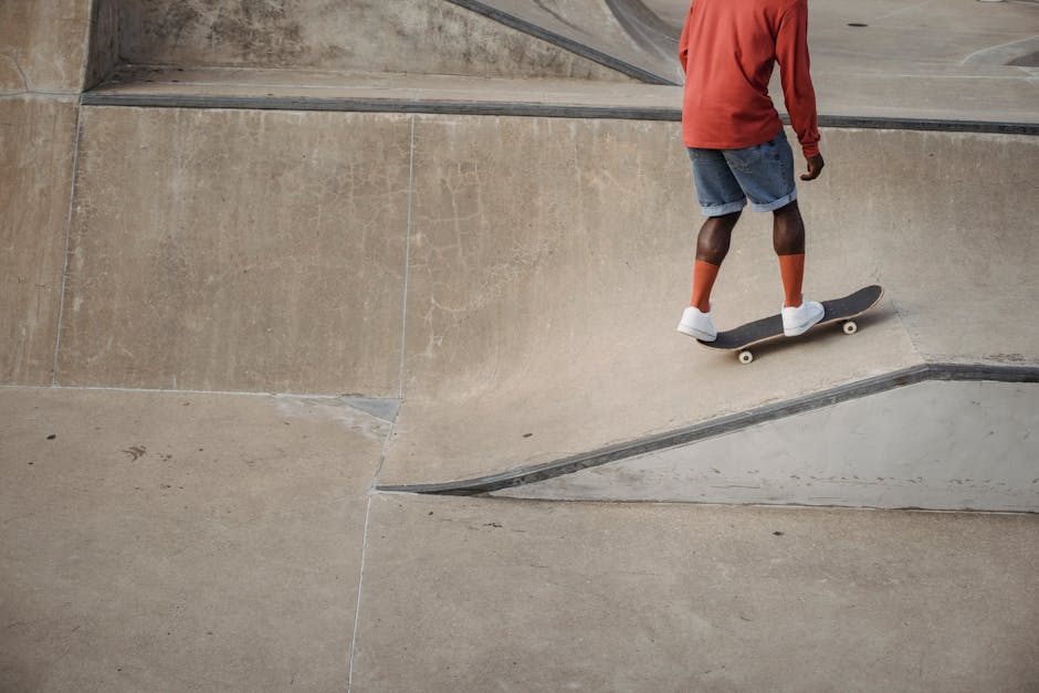 Crop unrecognizable African American skateboarder wearing red long sleeve t shirt and socks with white sneakers practicing stunts during training in skatepark in daytime