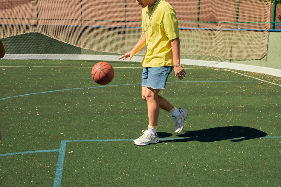 Adult male casually dribbling a basketball on a sunny outdoor sports court.