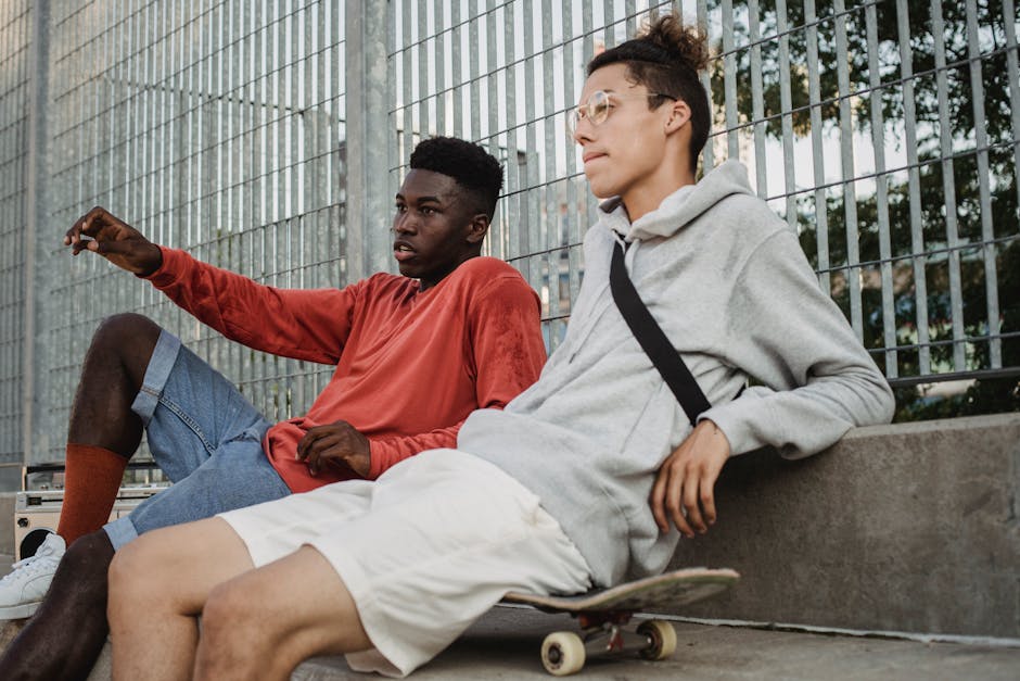 Serious multiracial young men talking to each other while sitting on skateboards in city park