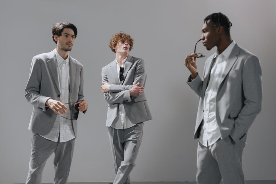 Three diverse young professionals in gray suits posed casually indoors.