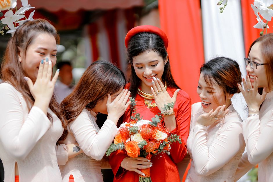 Positive young bride standing with friends and smiling while looking at hands on wedding day