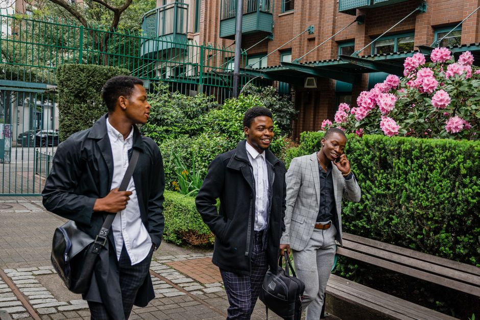 Three businessmen walking and talking on the phone in an outdoor garden area with blooming flowers.