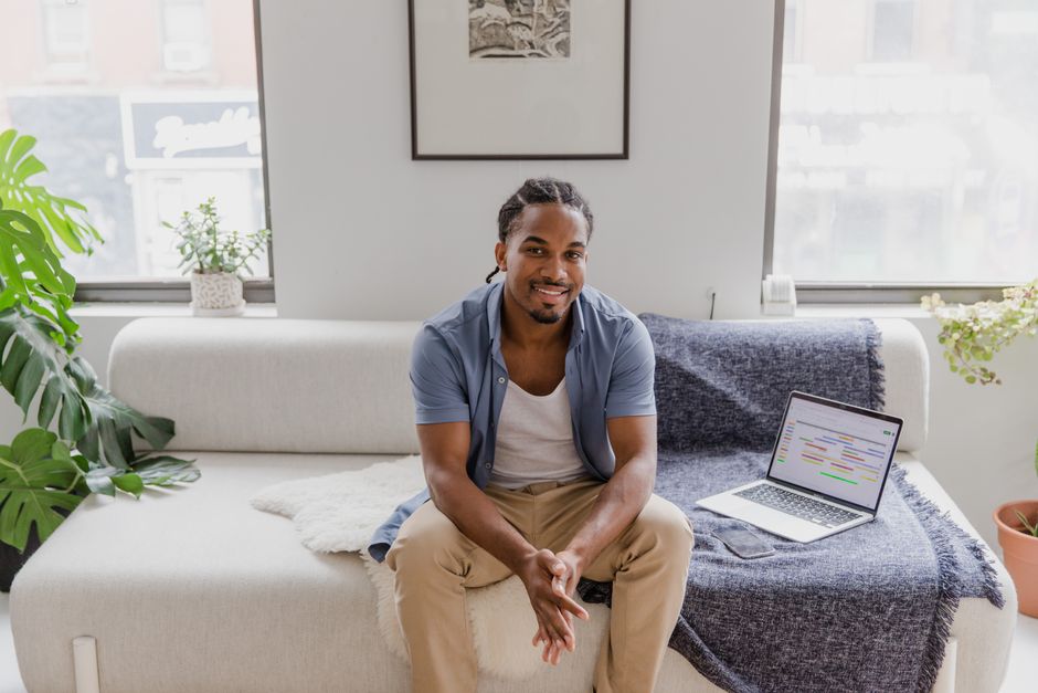A cheerful man sitting on a sofa in a home office with a laptop, radiating serenity and comfort.