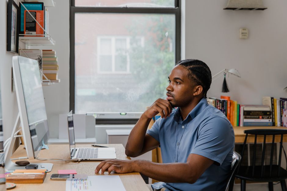 Adult man concentrating at his home office desk with computer, books, and natural light.