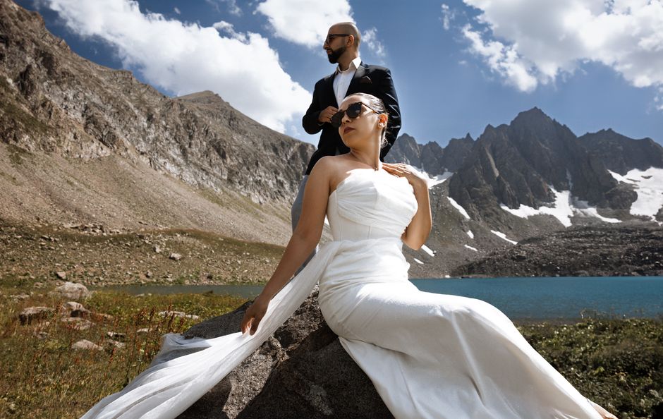 Elegant couple poses in white dress and suit against Syunik Province mountain landscape.