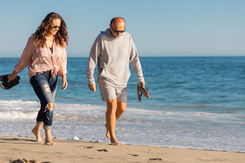 A senior couple enjoying a walk on the sandy beach in the warm summer sun.