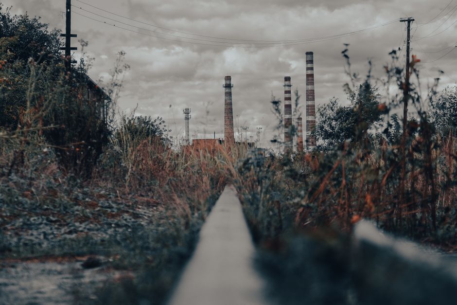 Moody view of tall chimneys rising above overgrown grass with dramatic clouds in Shebekino, Russia.