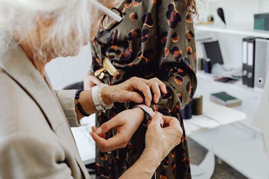 Elderly tailor taking dress measurements on a young woman in a fashion studio. Professional attire fitting.