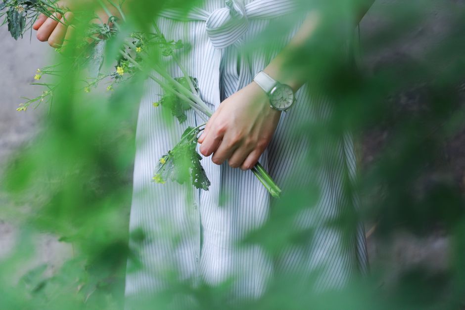 Close-up of a woman holding green foliage while wearing a striped dress outdoors.