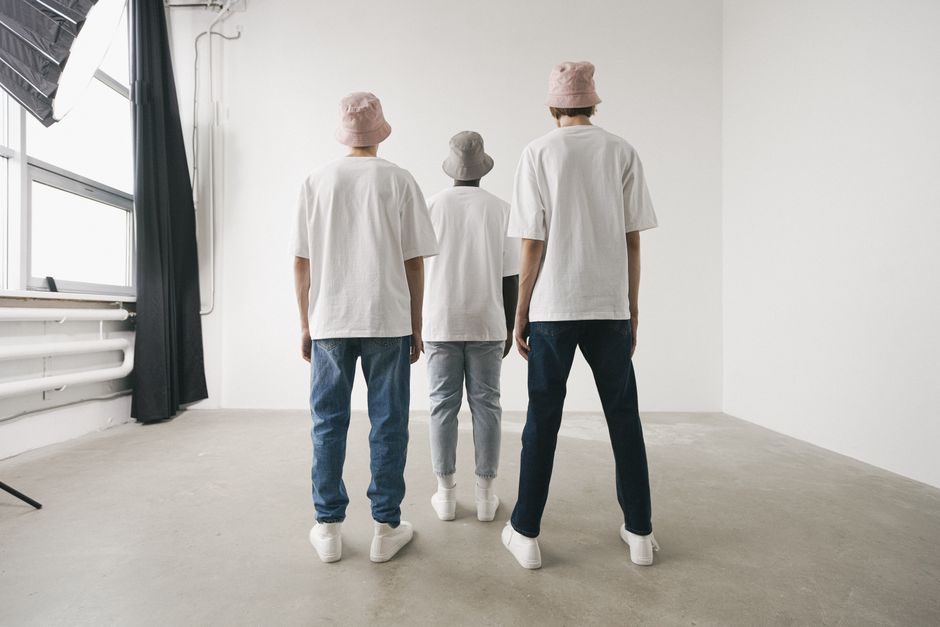 Three men in bucket hats and white shirts standing in a minimalist studio.