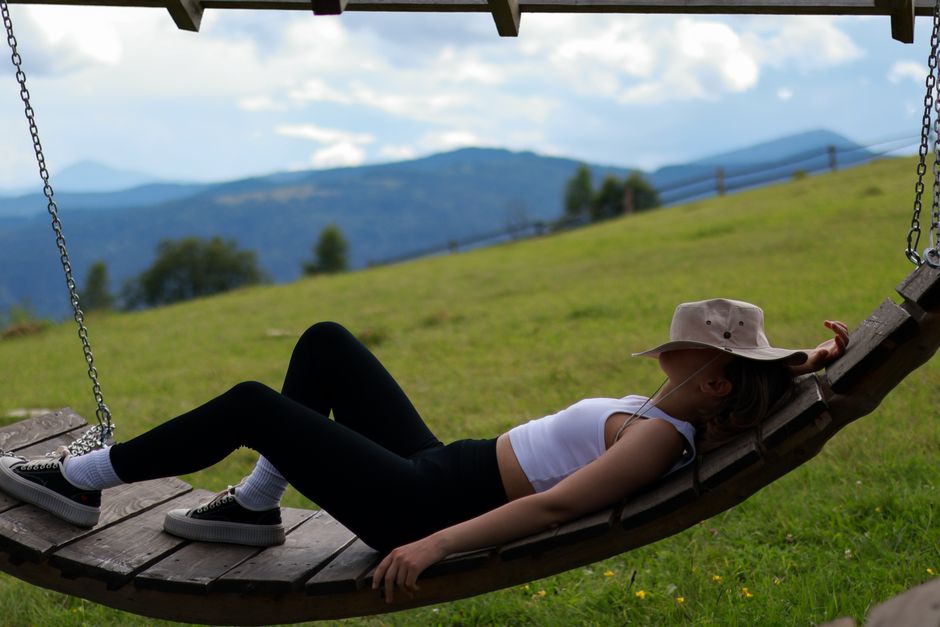 A woman enjoys a peaceful day on a wooden swing in a rural hillside setting.