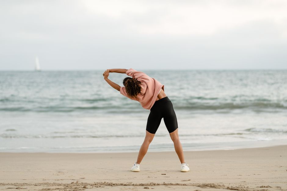 A woman stretching on the beach with a scenic ocean view at sunrise.