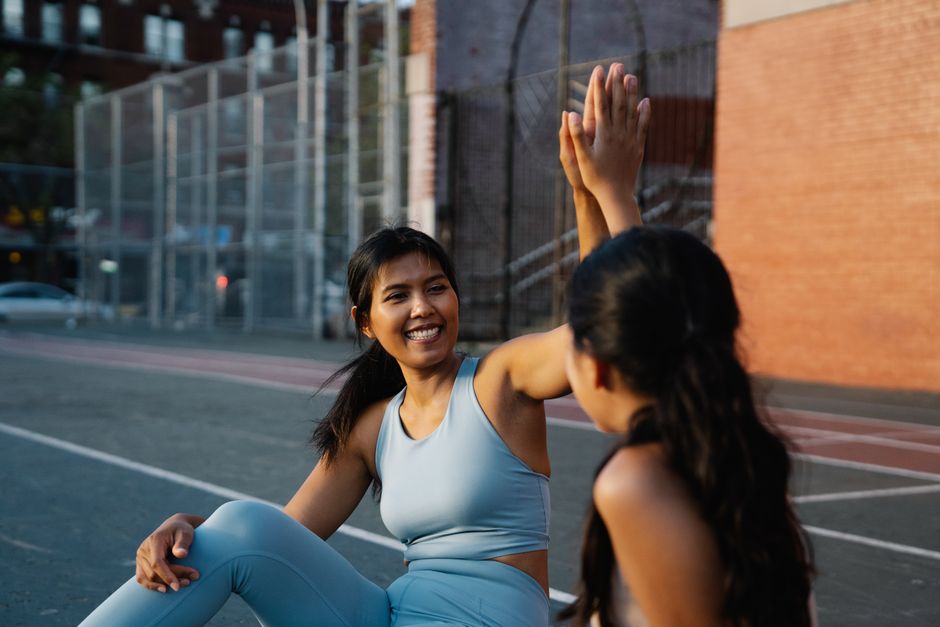 Two women in activewear high-fiving on a city street, exuding happiness and friendship.