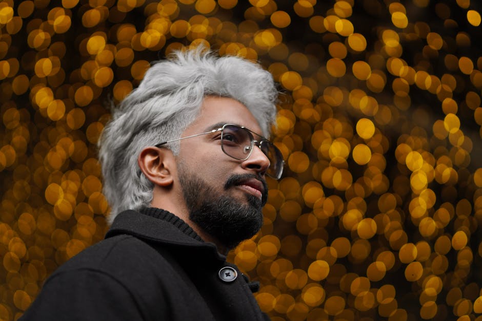 A striking portrait of a man with gray hair, black coat, and glasses, set against a warm bokeh backdrop.