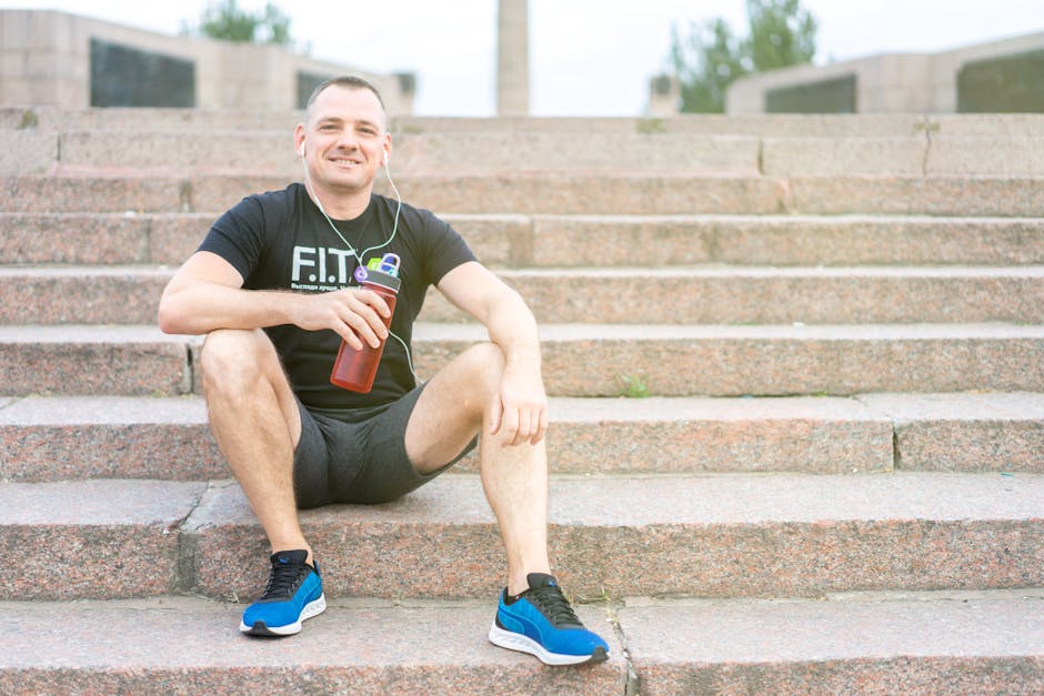 Smiling man in activewear sitting on stairs with a tumbler, enjoying a sunny day.