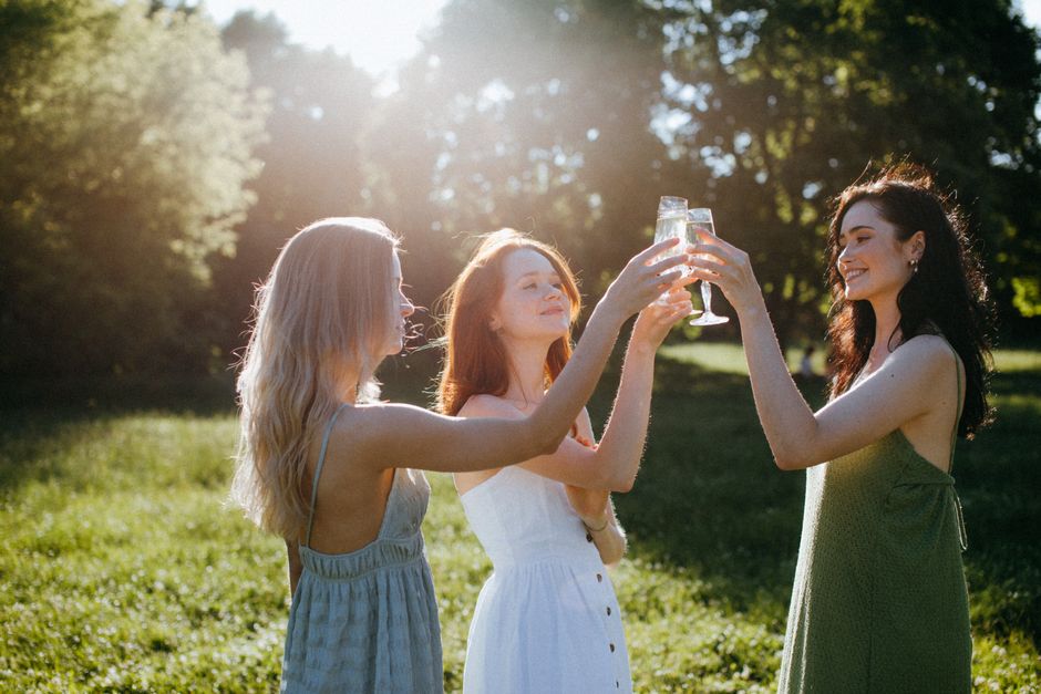 Three women celebrating friendship with a toast in a sunlit park.