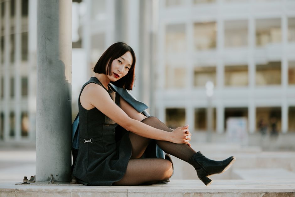 Elegant woman in black dress sitting outdoors against modern architecture.