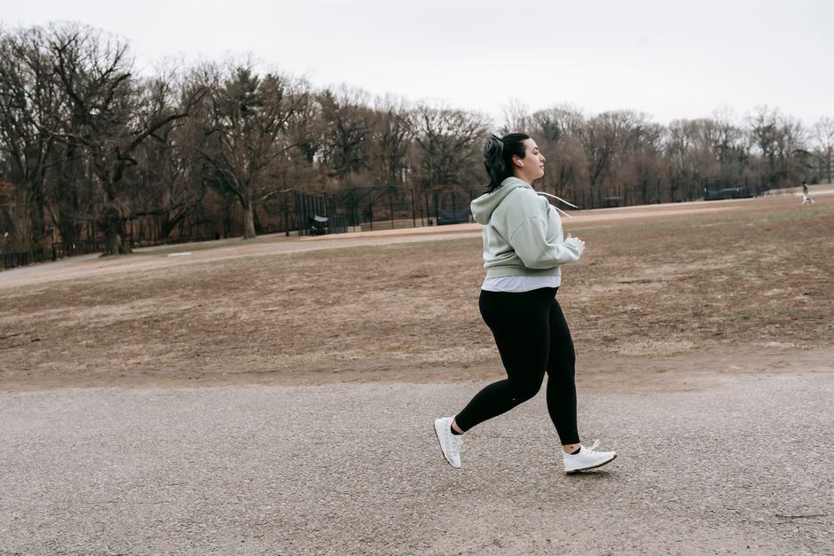 Side view of overweight young female jogging in park with leafless trees in autumn
