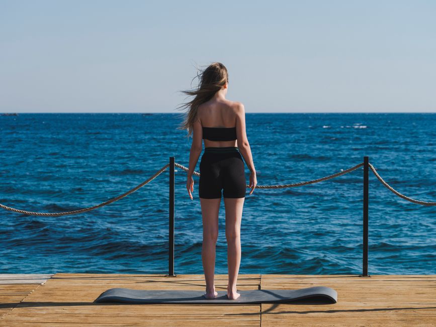 Woman in sportswear performs yoga by the sea on a sunny day.