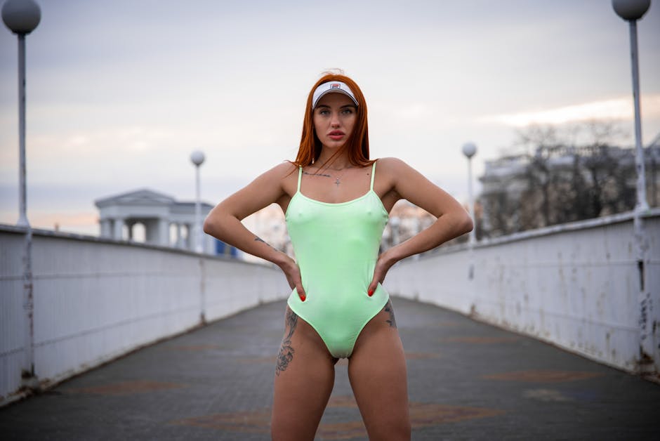 Young woman standing confidently in a neon swimsuit on a city bridge during the day.