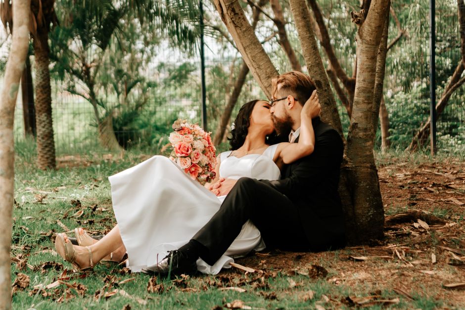Charming couple in wedding attire shares a romantic kiss under trees in a park.