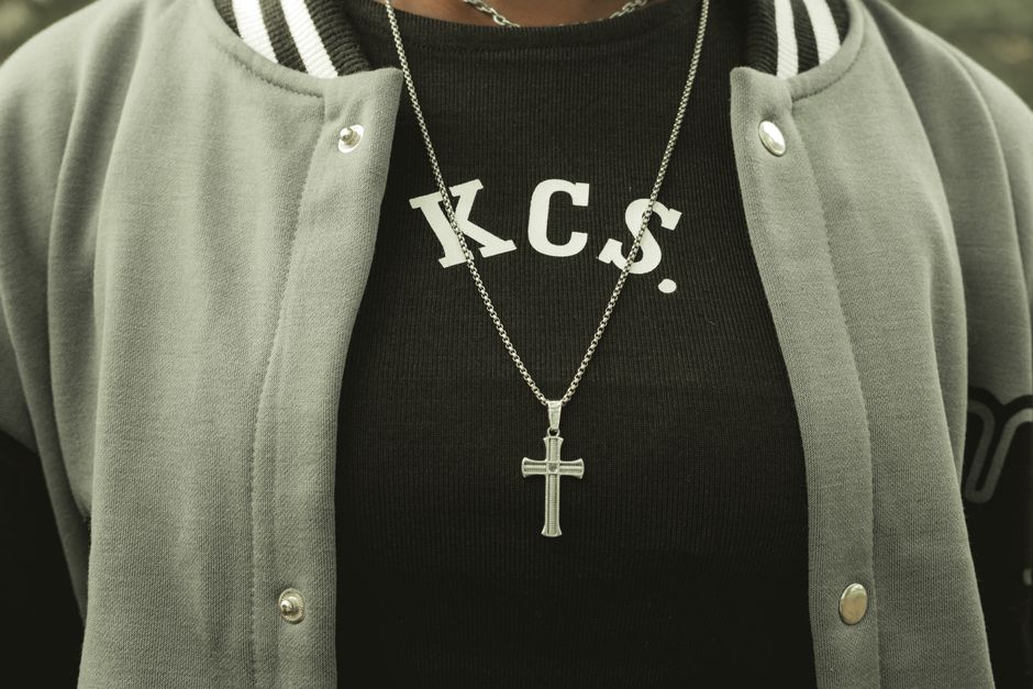 A stylish varsity jacket with a prominent silver cross necklace, displaying urban fashion.