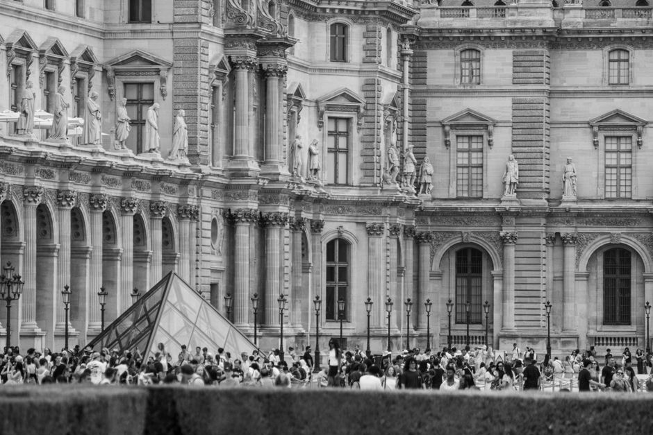 Monochrome image of the Louvre Pyramid surrounded by tourists in Paris, France.