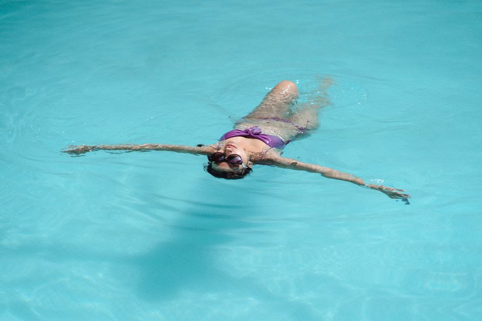 From above of unrecognizable young slim female tourist in bikini and sunglasses floating in swimming pool on sunny summer day