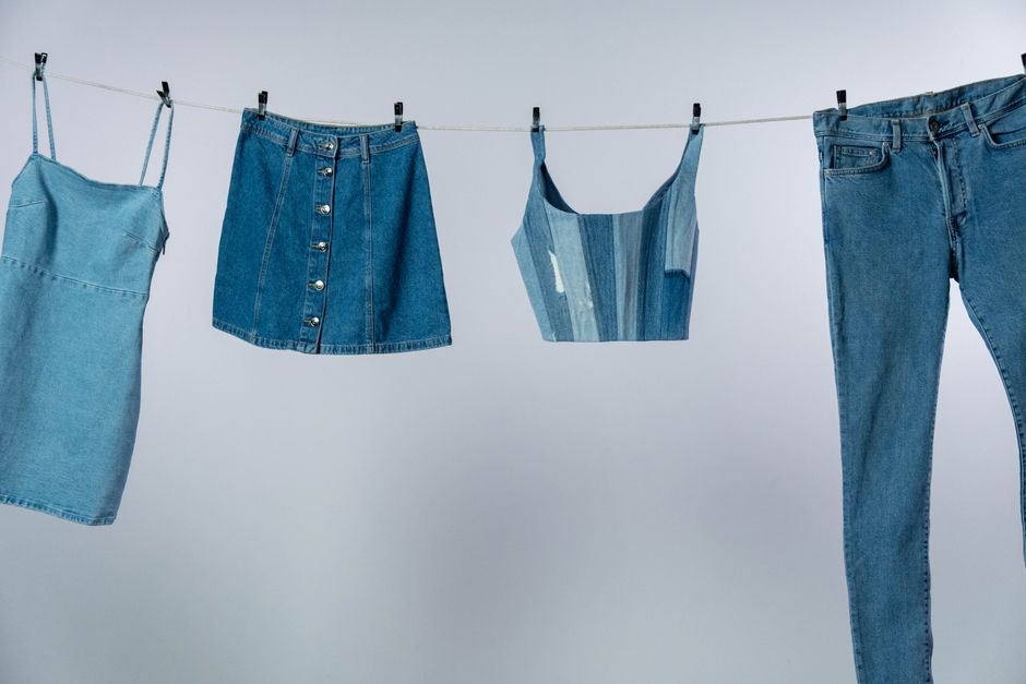 Various denim garments drying on a clothesline against a neutral background.