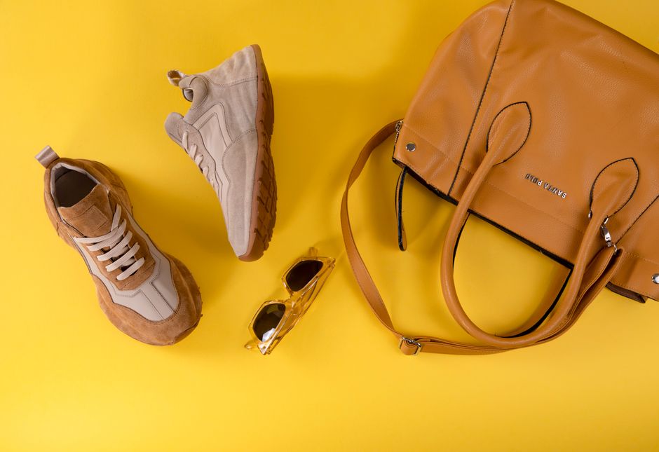 Stylish brown handbag, fashionable eyewear, and sport shoes on vibrant yellow background.
