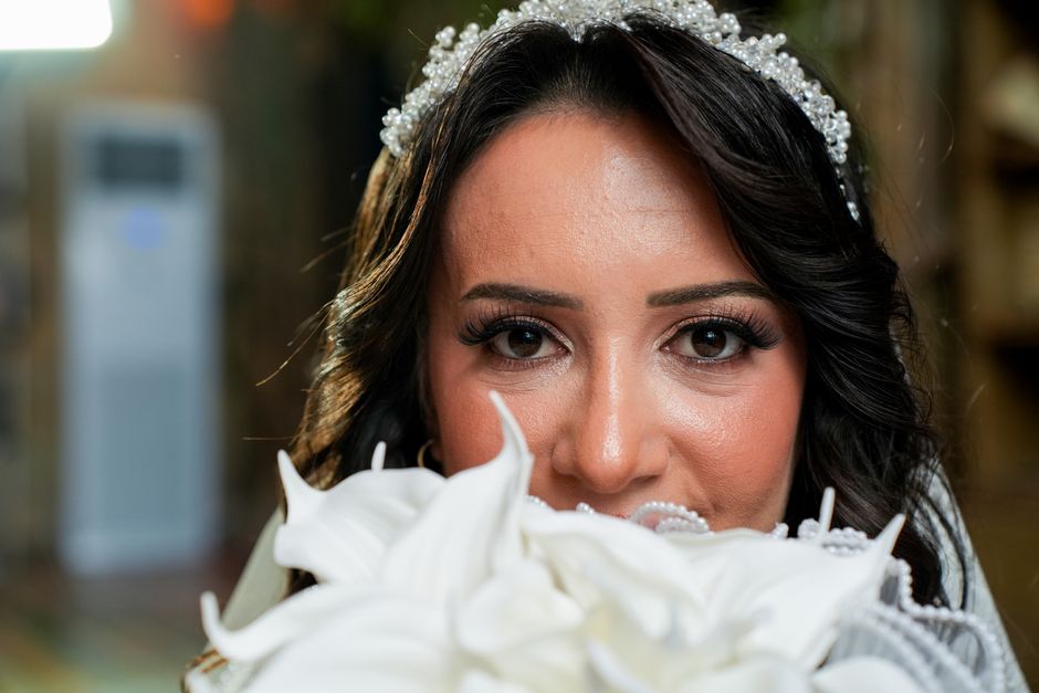 Close-up of a bride holding a white bouquet, showcasing elegant makeup and a pearl headpiece.