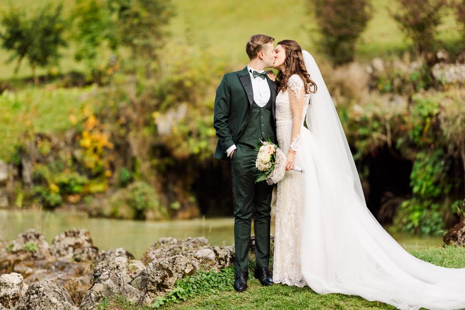 Bride and groom share a romantic kiss in lush Bușteni, Romania garden setting.