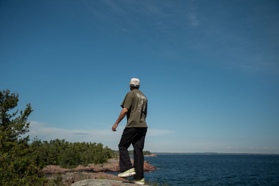 A man gazes at the ocean from a rocky cliff with a clear blue sky above, capturing tranquility and freedom.