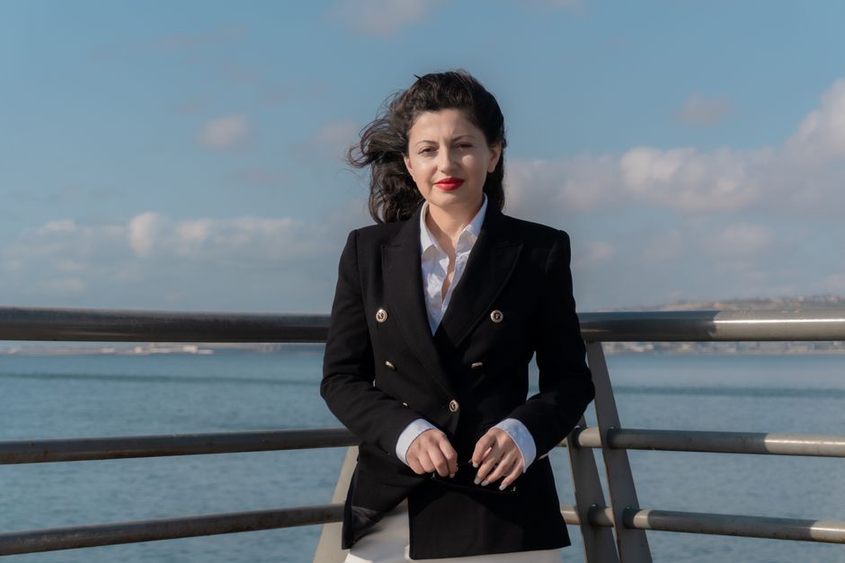 Confident woman in a black blazer poses by the seaside in Baku, Azerbaijan.