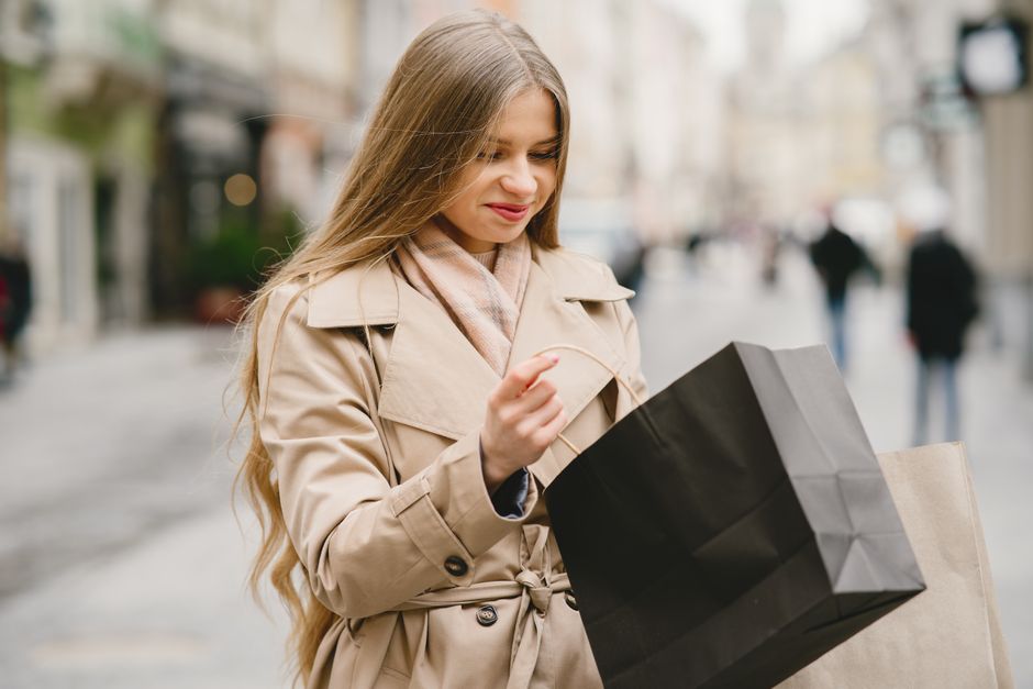 Caucasian woman smiling outdoors with shopping bags in winter attire.