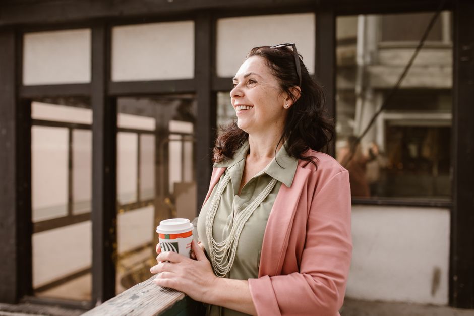 Mature woman happily holding coffee outdoors in an urban setting.