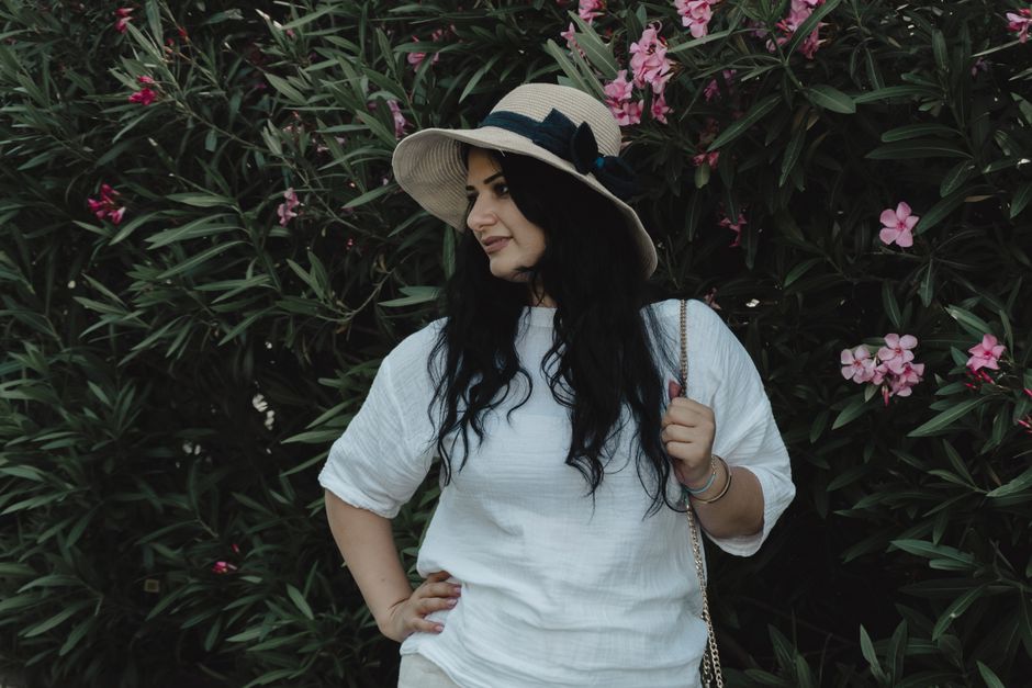 A woman in a white shirt and hat stands by a blooming oleander bush in Baku.