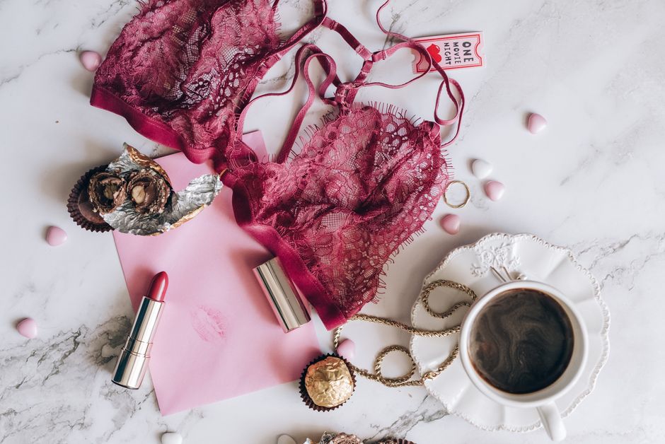 A romantic flat lay with lace lingerie, coffee, chocolates, and a lipstick on a marble surface.