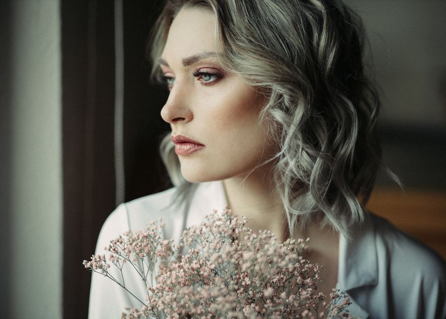 Thoughtful young crop female with wavy hair and makeup standing with bouquet of Gypsophila flowers