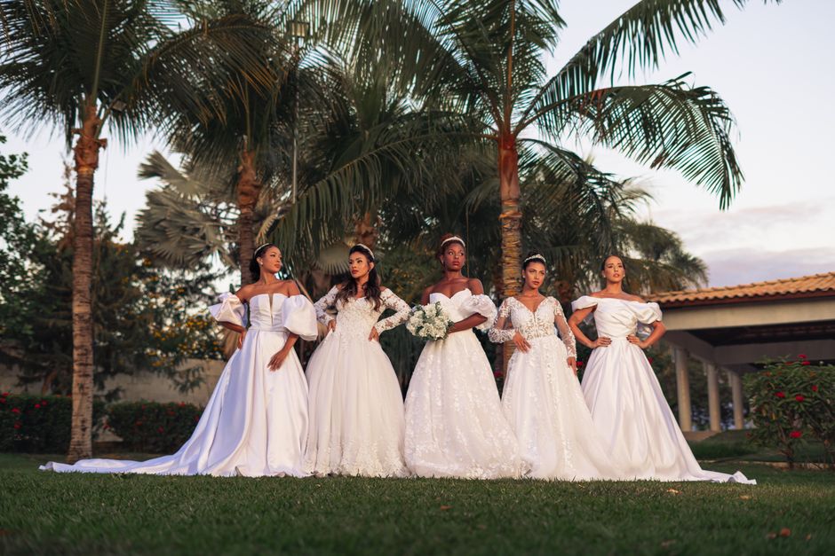 A group of bridesmaids in elegant white gowns posing outdoors amidst palm trees.