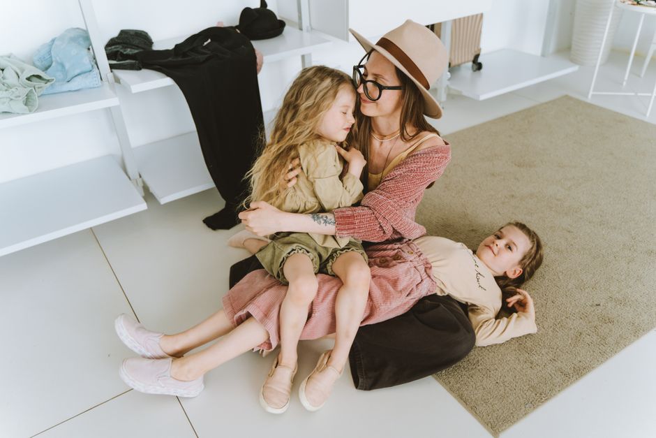 A mother lovingly embraces her two daughters in a cozy indoor setting, showcasing family togetherness.