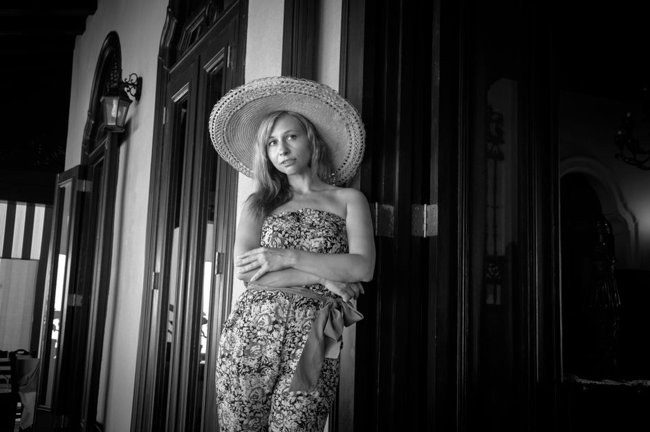 Stylish woman in vintage floral attire and wide-brimmed hat posing indoors, exuding retro fashion elegance.
